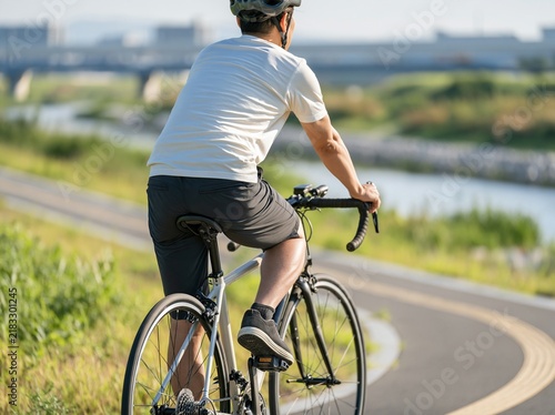 Fototapeta 天気の良い川沿いのサイクリングロードを快走する自転車の男性の後ろ姿