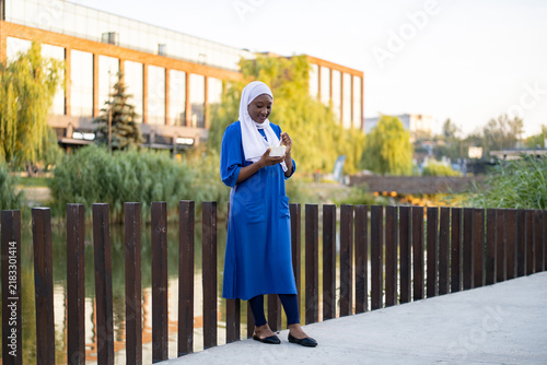 Bild auf Leinwand A young African American Muslim woman wearing a hijab and a blue dress enjoys a