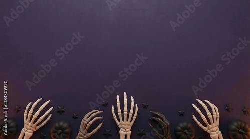 Ceramic skeleton hands and small pumpkins on a dark purple background for Halloween