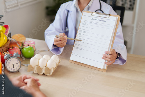 Nutritionist pointing at health summary chart during patient consultation for healthy diet plan