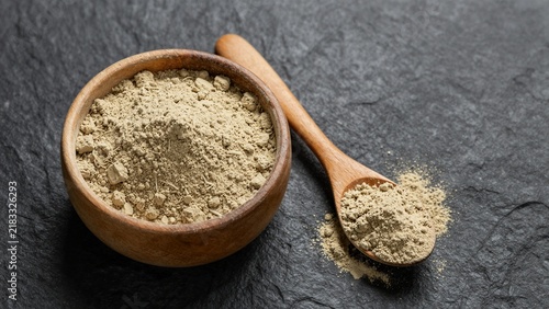 Organic maca root powder displayed in a wooden bowl with spoon on dark stone surface, highlighting natural nutrition and wellness.
