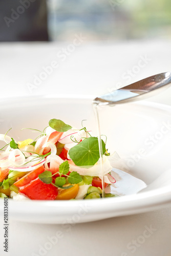 Gourmet summer salad with tomatoes, strawberries, and fresh herbs in a white bowl. Fine dining restaurant dish isolated on white background