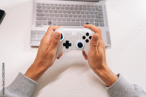 Obraz na płótnie Person playing video game on laptop with wireless gamepad, focusing on screen while engaging in online multiplayer action and live streaming