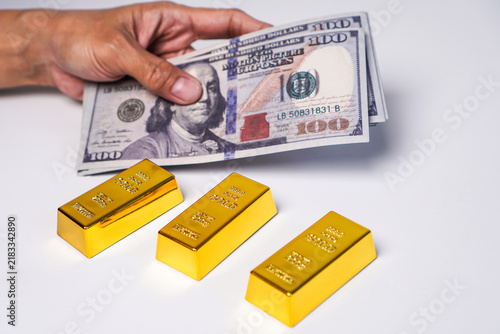 Картината върху платно A hand holding a stack of US$100 banknotes and three gold bars.