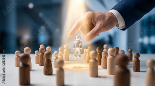 A business professional hand selecting a special worker from a group of wooden figures to represent talent management recruitment processes and leadership human resources decision making