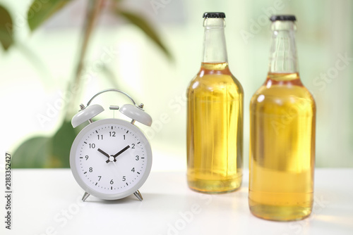 Фотография White alarm clock stands beside two amber glass bottles on bright tabletop, with
