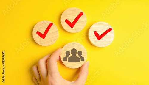 Hand holding a wooden block with a group of people icon surrounded by check marks on a yellow background