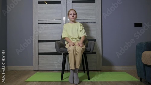 Young girl performing chair exercises at home, focusing on leg movements for fitness and health improvement, an indoor workout routine for children and youth.