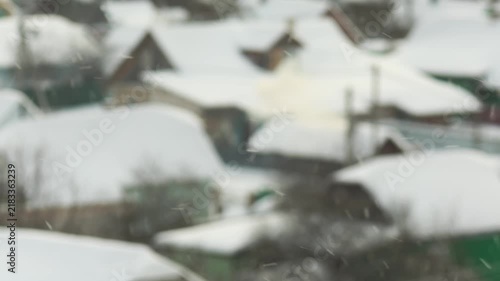 Winter scene of snow falling over village landscape, rooftops of houses covered in thick layer of white snow, creating peaceful wintertime atmosphere, slow motion