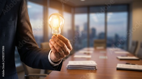 Businessman holding glowing light bulb in modern office, representing swift innovation and creative business solutions for successful corporate growth and leadership vision.