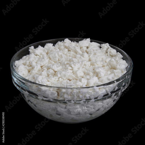 Cottage cheese in glass bowl isolated on black background. Side view of Creamy dairy curds