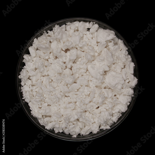 Cottage cheese in glass bowl isolated on black background. Top view of Acidic cultured curd