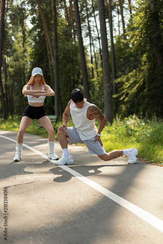 Quadro su tela Fit young couple doing warm-up stretching exercises on a sunny park path outdoors