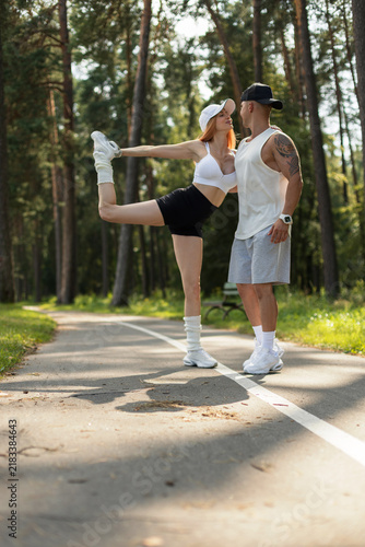 фотографія Fit young couple doing partner yoga and stretching outdoors on a park path surrounded by pine trees