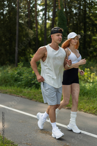 Bild auf Leinwand Active young couple jogging together on a park path surrounded by green forest