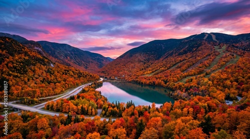 Winding road and mountain lake surrounded by autumn forest during a vibrant sunset over the valley with foliage