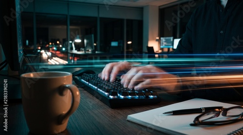 Person typing on a computer keyboard in a dark office at night with motion blur light trails with types backlit