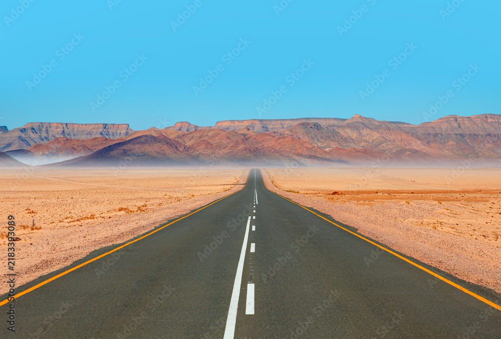 Obraz premium Beautiful empty asphalt dirt road in desert plain with mountains in background - Namibia, Africa