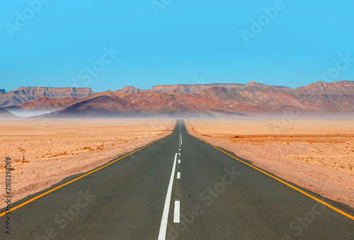 Beautiful empty asphalt dirt road in desert plain with mountains in background - Namibia, Africa