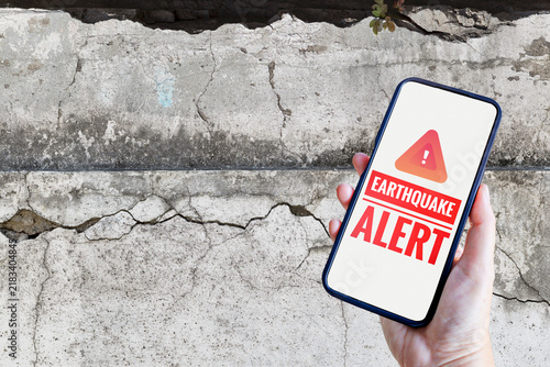 Earthquake alert on smartphone over crack wall background, emergency aleart, Natural Disaster warning