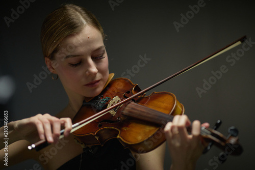 Young adult Caucasian woman playing acoustic violin with eyes closed during rehearsal. Visual suitable for classical music education, performing arts marketing, concert promotion campaigns