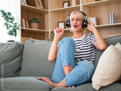Cheerful woman listening to music and moving to the rhythm while relaxing comfortably on the couch.