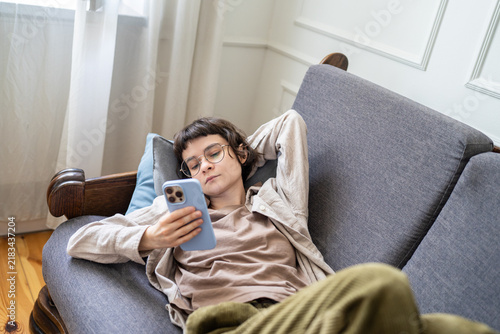 Foto Woman lying on sofa scrolling smartphone instead of completing tasks