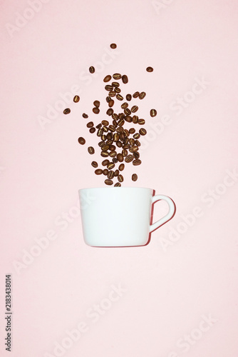 Roasted coffee beans fall into a white cup on a pink background