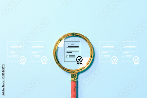 Magnifying glass highlights an approved certificate among documents, symbolizing verification, quality control, audit, compliance and certification on a blue background with copy space.
