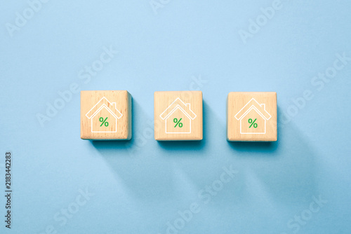 Three wooden blocks with house and percent symbols represent mortgage rates, home loans and real estate finance on a blue background with copy space for banking concepts and investment.