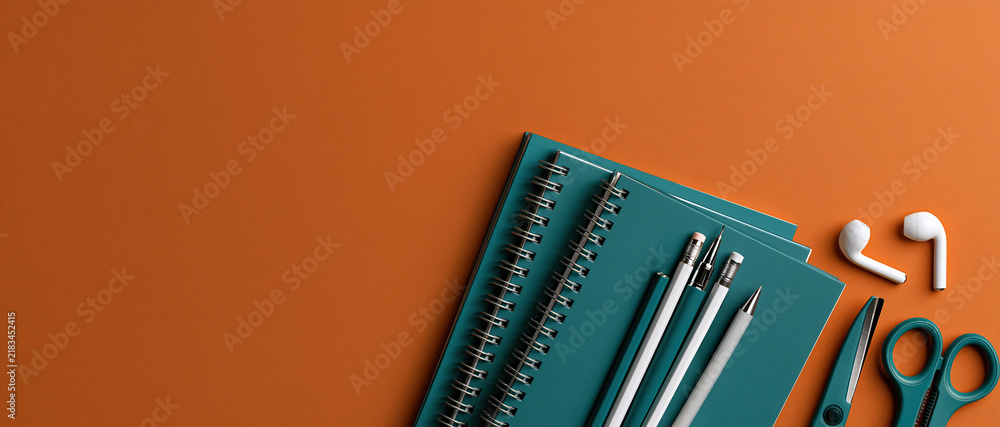 Obraz premium Vibrant backtoschool flatlay featuring teal spiral notebooks, pens, pencils, scissors, and wireless earbuds on bold orange. Perfect for education campaigns, student lifestyle, or.