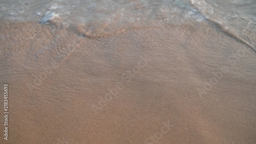 Gentle ocean waves washing over a sandy beach at sunrise or sunset