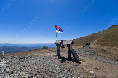 Bild auf Leinwand Wooden bell structure with Serbian flag on mountain summit under blue sky