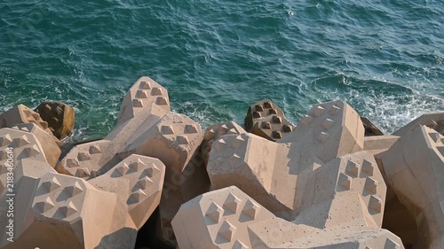 Concrete tetrapods protecting coastline from crashing ocean waves on a sunny day