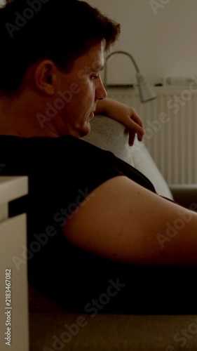 DEPRESSION: Young adult man sits thoughtfully on a sofa in a dim room at home. Alcohol nearby