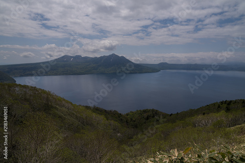 Fotografie Deep caldera lake framed by green ridges and volcanic peaks