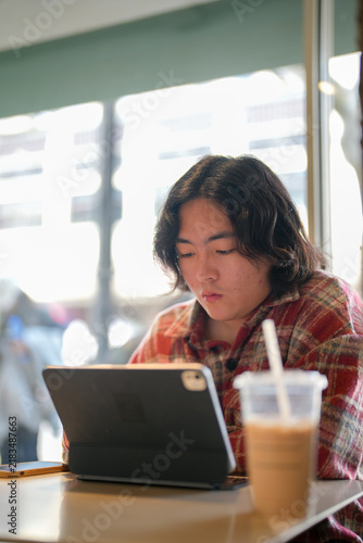 Photography A vertical side view shows a person reading from a tablet with an iced drink on the table