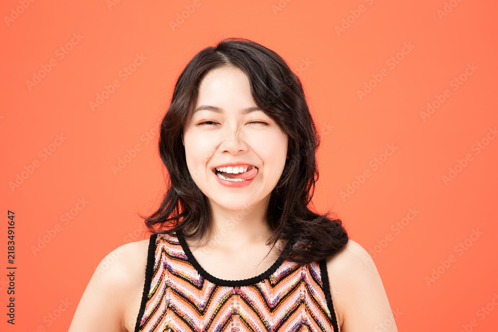 Fototapeta premium Young woman playfully sticking tongue out and winking on orange background