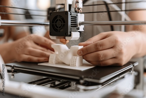 Obraz na płótnie Close up of hands operating a 3D printer creating a white plastic prototype model