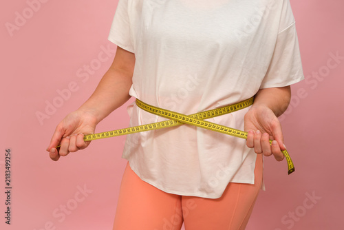 Quadro su tela Woman measuring waist with yellow tape measure on pink background