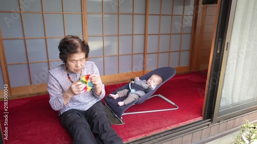 A seated person holds a colorful patterned ball near an infant reclining in a bouncer at an open doorway.