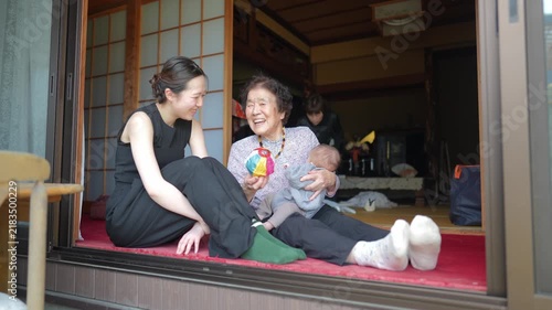 Two adults sit on the red threshold area with an infant, while a colorful ball rests nearby.