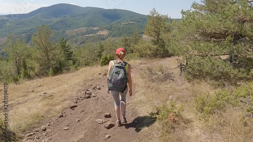 Fit senior woman carrying a backpack, in great shape and excellent physical condition, hiking on the mountain path. Concept of active aging and healthy lifestyle. 