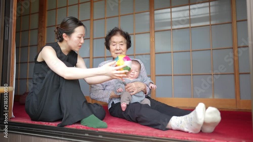 Two seated adults interact with an infant as a multicolor fabric ball hangs in midair in front of sliding doors.