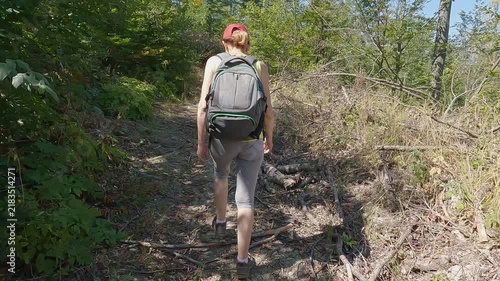 Fit senior woman carrying a backpack, in great shape and excellent physical condition, hiking on the mountain path. Concept of active aging and healthy lifestyle. 