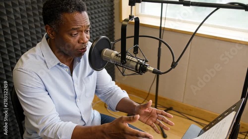 Reading script starting man in light-blue shirt speaking into mic on boom arm at studio, gesturing