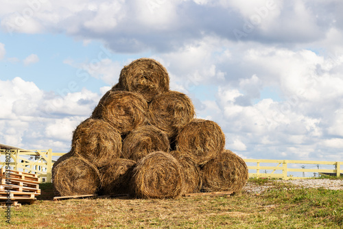 round hay bales are stacked in a pyramid beneath dramatic summer clouds, presenting harvested livestock feed, rural agriculture, seasonal work and food security