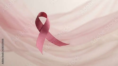 Pink awareness ribbon resting on a soft draped fabric background with awareness feminine prevention medicine