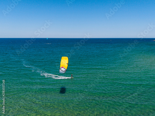 Aerial view of a kitesurfer gliding across the turquoise sea with a bright yellow kite under a clear blue sky in Lozenets, Burgas, Bulgaria.