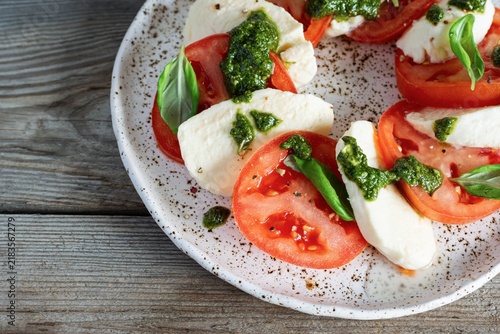 Caprese salad with juicy tomatoes, fresh mozzarella and pesto. Concept for a tasty and healthy appetizer, flat lay. Italian food, cuisine.